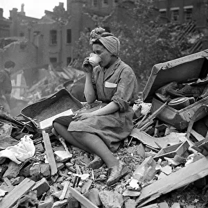 A woman enjoys a cup of tea in the midst of the bomb damage at New Cross after air raids