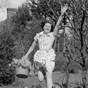 A woman leaping for joy with a basket full of daffodils picked from her garden on a