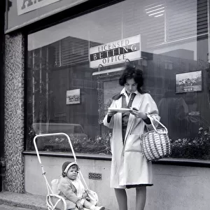 A woman punter studies the form guide outside A E Fane and Co betting shop in islington