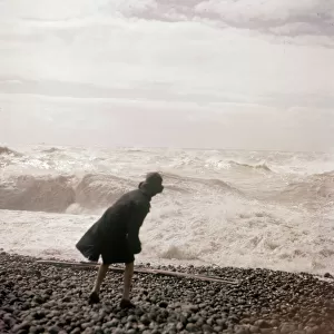 A woman throws one of the many beach pebbles in to the rough sea on the Sussex coast