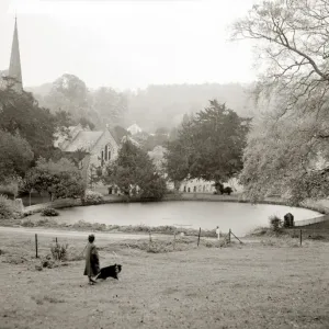 A woman walking her border collie dog in the countryside Lake church trees field