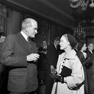 Woman wearing long coat and hat talking to a man wearing a suit at a cocktail Party