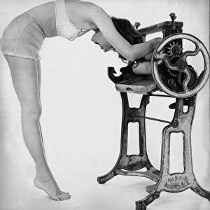 A woman wearing underwear drying her through an old fashioned roller machine