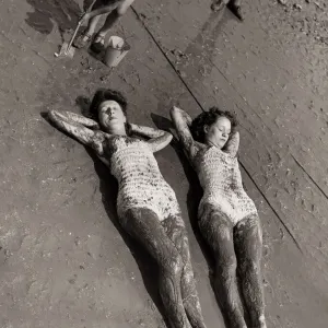 Women Holidaymakers sunbathing on the wet sand wearing swimming costumes bathing suits