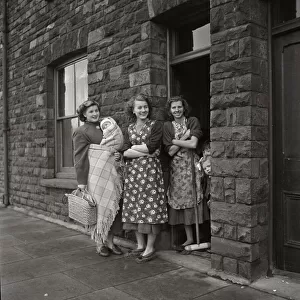 Three women standing gossiping on the street outside terraced housing in Cardiff, Wales