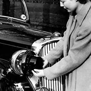World War II: Blackout. Woman fitting blackout shields to the headlamps of her car