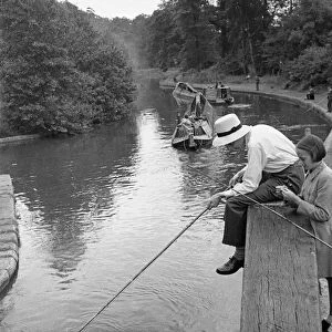 A young angler wearing a panama hat fishing in the Grand Union Canal between