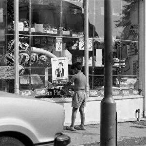 A young boy puts up a Muhammad Ali poster on a shop window in Birmingham