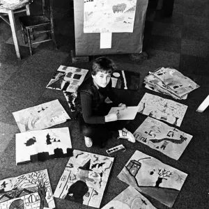 A young boy sitting on the floor among paintings and drawings which have been made by