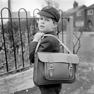 Young boy wearing school uniform carrying a satchel on his shoulder