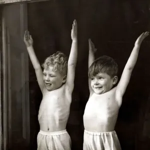 Two young boys doing stretching and breathing exercises in front of an open window Two young boys doing stretching and breathing exercises in front of an open window