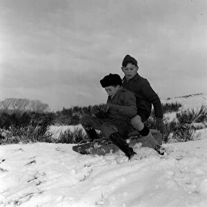 Two young boys riding their sledge down a snow covered hill January 1960