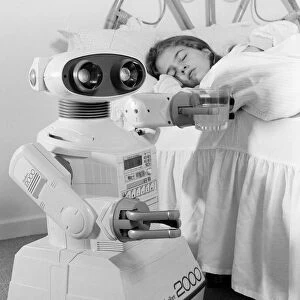A young girl in bed being woken by an Omnibot 2000 toy robot. 21st October 1986