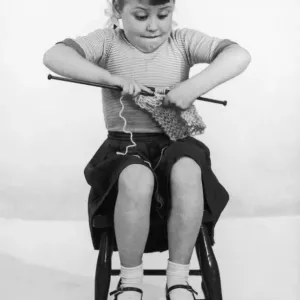 A young girl concentrating on her knitting, biting her lip sticking her elbows well out