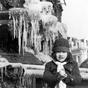 A young girl freezing cold, wrapped up in a coat, hat and scarf