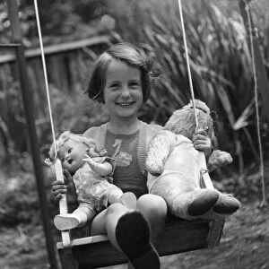 Young girl sitting on her swing in the back garden with her favourite toys