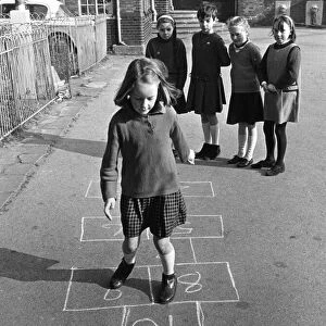Young Pgirl playing a game oh hopscotch with her friends in the school playground