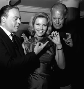 Actors Herbert Lom, Honor Blackman and Curt Jurgens holding thread of cotton which in