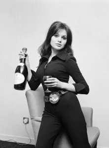 Actress Madeline Smith holding a glass of wine and bottle of champagne at a BBC Press