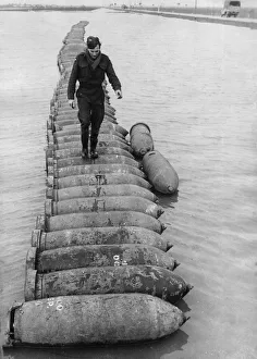 00072 Prints: An airman using a line of 1000 lb bombs as a bridge to cross a flooded airfield at an RAF