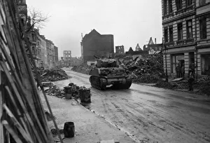 An American tank rumbles through a wreckage lined street on the outskirts of