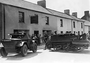 Armoured vehicles of the local Home Guard are flung across the High Street of a un-named