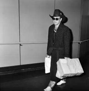 01323 Prints: The arrival of Elton John at Heathrow Airport carrying Christmas presents from a buying