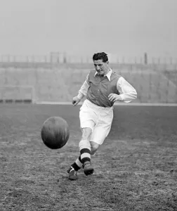 Arsenal Football player Ronnie Rooke kicking football with the north bank terracing