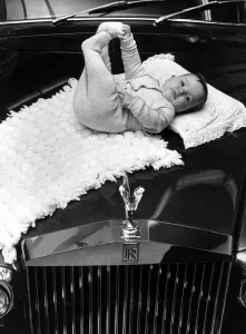 A baby girl lying on a mat on the bonnet of a Rolls poyce Silver Cloud car November