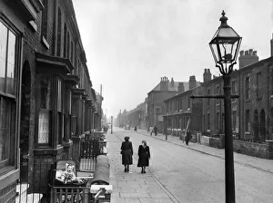 Street Lamp Prints: A baby sits in its pram outside the front of a house in a terraced street in the Cheetham