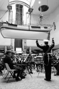 Musicians Prints: A band plays beneath a replica of Captain Cooks ship Endeavour