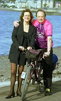 Folk Prints: Barbara Dickson wearing glasses and a black suit poses with James Bolam on a bicycle in