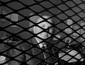 Bookmaker Sidney Glanz pictured through the grill inside his betting shop in the Isle of