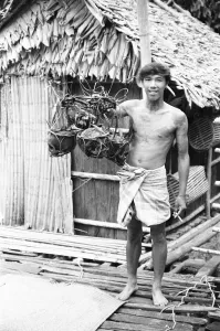 Asia Prints: A Borneo headhunter tribesman seen here holding up a basket of human skulls