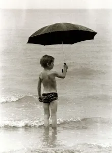 Boy paddling in the sea in the rain holding up an umbrella in Clacton Essex. 1980
