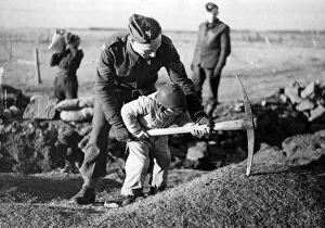 Digging Prints: British troops in Iceland. A young child helping a soldier pickaxe the ground. Circa 1941