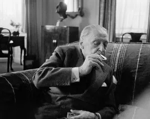 British writer William Somerset Maugham photographed smoking a cigarette at his home