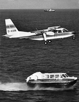 Hovercraft Prints: A Britten Norman Islander aircraft flies over a Cushion Craft Hovercraft