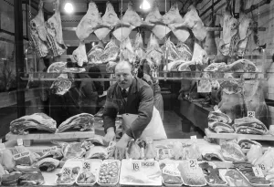Butcher standing in his shop window, showing off his various meat products currently