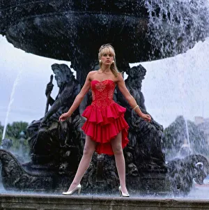 Occupation M Prints: Carol Smillie model TV presenter wearing red dress standing ion front of a water fountain