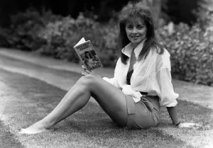 Carol Vorderman TV Presenter sitting on grass lawn holding paperback book