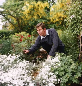 Christopher Ravenscroft Actor crouching down in his garden looking at a rose bush