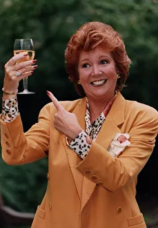 Cilla Black holding glass of wine wearing gold jacket and spotted blouse
