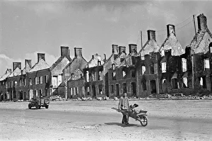 Jeep Prints: A civilian pushes a wheelbarrow of salvaged belongings amidst the ruined buildings