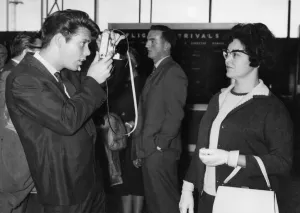 00781 Prints: Cliff Richard taking a picture of his Mother at London Airport before leaving for New