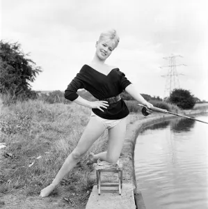 Clothing: Fashion: Beachwear: Model by the river bank fishing. August 1963 E490-004