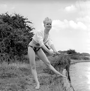 Clothing: Fashion: Beachwear: Model by the river bank fishing. August 1963 E490-017