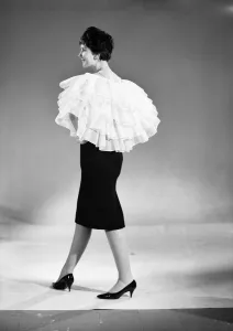 00435 Prints: Clothing: Fashion: Capes: Woman wearing frilly cape that can be adapted to become a skirt