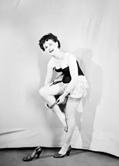 Clothing: Fashion: Underwear: Woman wearing corsett placing bow in hair. 1959