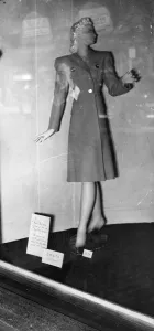 Female Prints: Clothing - A manikin in shop window displaying a coat for sale. Spring fashions